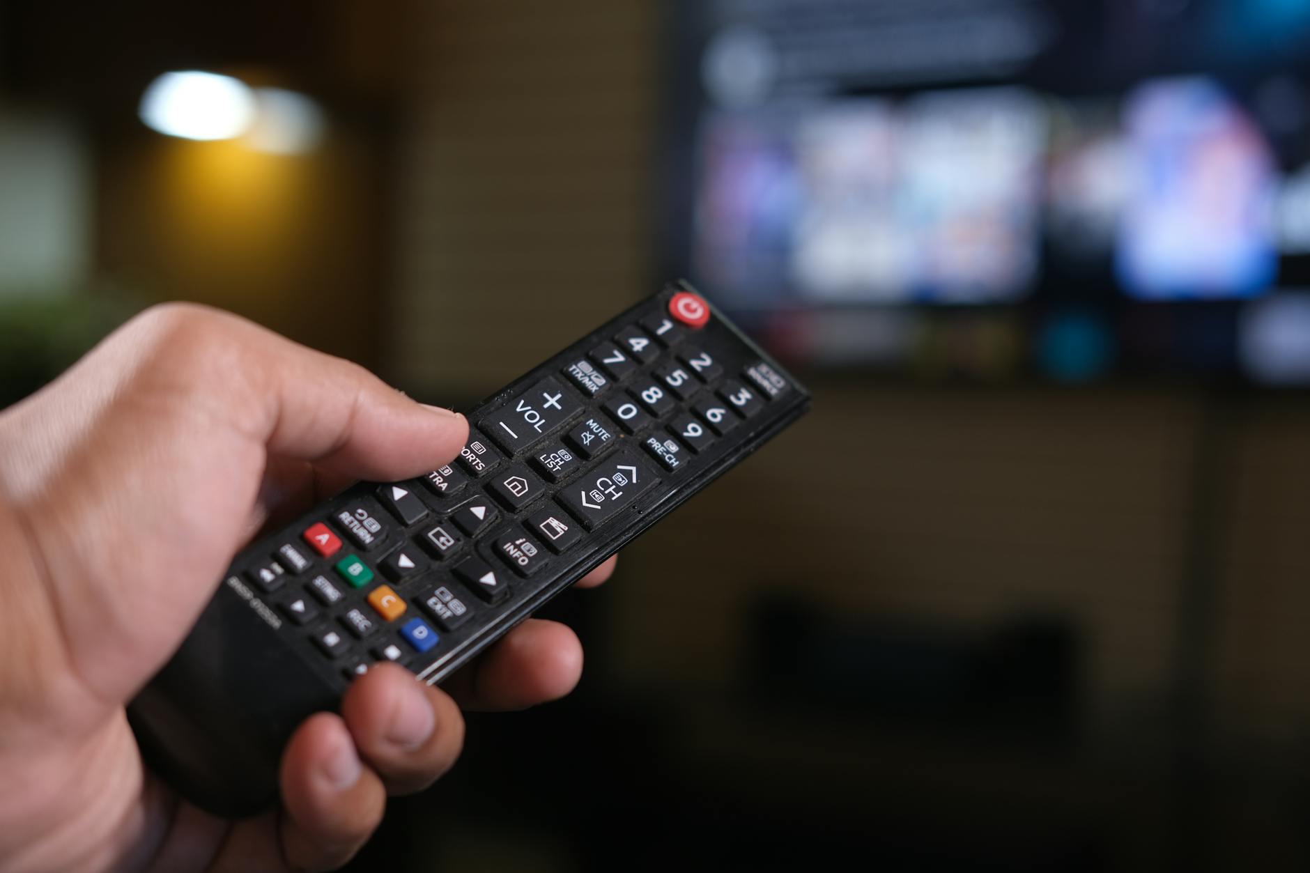 Hand holding TV remote with multiple streaming service options displayed on screen