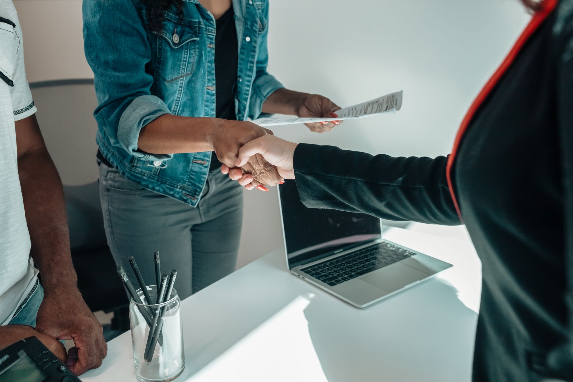 Two businesspeople shaking hands across a conference table during a deal signing
