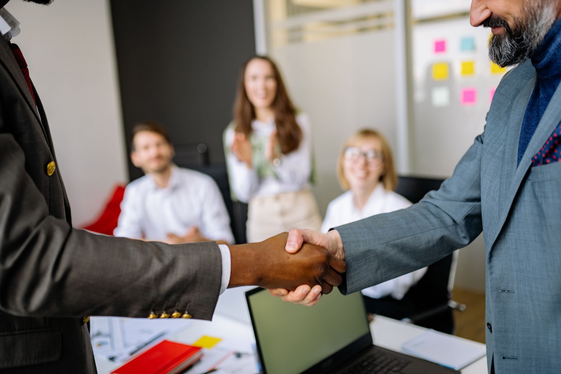 Two business professionals shaking hands across a conference table during a deal meeting